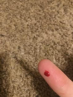 a finger with a red substance on it sitting next to a brown carpeted floor