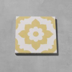 a yellow and white tile with a flower design on the bottom, against a gray wall