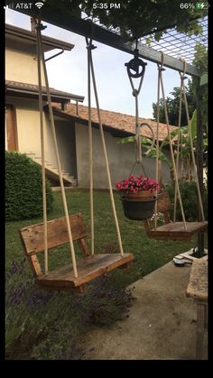 two wooden swings in front of a house with flowers on the ground and one swing is empty