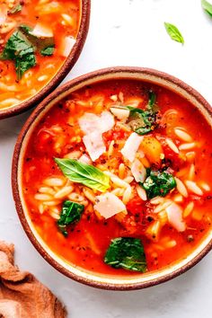 two bowls filled with pasta and spinach soup on top of a white countertop