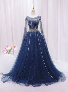 Aeonian elegance embodied in a dress, this blue gown is truly breathtaking! Capturing the essence of celestial beauty, it boasts an intricate overlay of sparkling sequins and delicate beading that illuminates the deep blue fabric beneath. The gown's fitted bodice highlights a sophisticated silhouette, cinched at the waist with a band of embellishments that enhance its figure-flattering design. Long, sheer sleeves and a gently scooped neckline add a touch of royal grace, perfect for a prom queen. The expansive skirt, speckled with glimmers like distant stars, flows into a soft, sweeping hem, making every movement a statement of grace and poise. This dress is designed for those who dream of a magical evening, wrapped in glamour and inspired by the night sky. Dark Blue Fantasy Gown, Sapphire Ball Gown, Starfall Ball Gown, Dark Blue Fantasy Dress, Royal Blue Gowns Elegant, Royal Blue And Gold Dress, Galaxy Wedding Dress, Blue Fantasy Dress, Royal Blue Dress Outfit