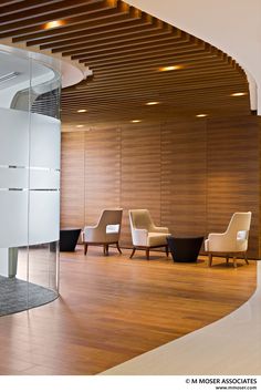 an empty lobby with chairs and tables in the center, next to a curved wooden wall