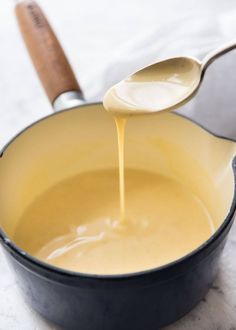 a wooden spoon is pouring liquid into a skillet