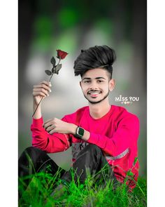 a young man is sitting in the grass holding a rose