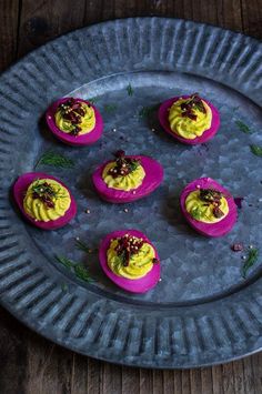 small deviled eggs with yellow and red toppings on a blue plate sitting on a wooden table