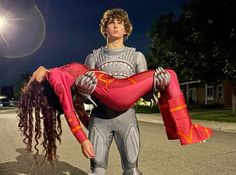 a man is holding a woman in his arms on the street at night with bright lights behind him