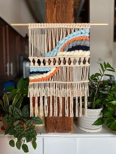 there is a wall hanging made out of yarn and wood with plants in the background