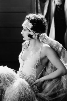 a black and white photo of a woman in costume with feathers on her head, looking off to the side