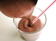 a person pouring chocolate into a glass with two straws in it on a white surface