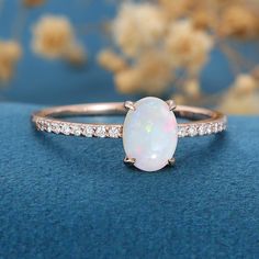 a white opal and diamond ring sitting on top of a blue surface