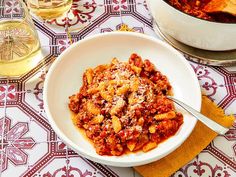 a bowl filled with pasta and sauce on top of a table next to a glass of wine