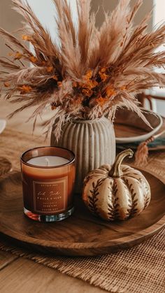 a candle sits on a plate next to some pumpkins and pamodia in a vase