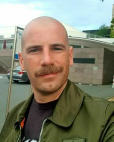 a bald headed man with a moustache on his face standing in front of a building