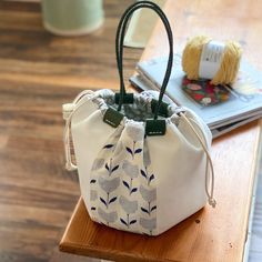 a white bag sitting on top of a wooden table next to a ball of yarn