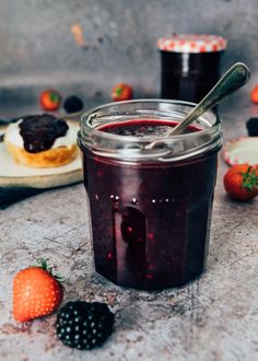 a glass jar filled with jam next to some berries and other fruit on the table