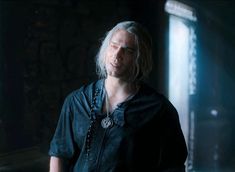 a man with long white hair wearing a black shirt and looking off into the distance