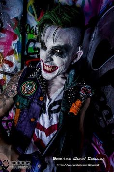 a man dressed up as the joker with tattoos and piercings on his arm, standing in front of graffiti covered wall