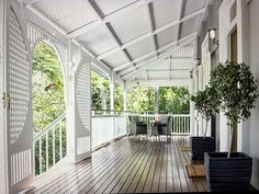 the porch is covered with white pergolated walls and wood flooring, along with potted plants