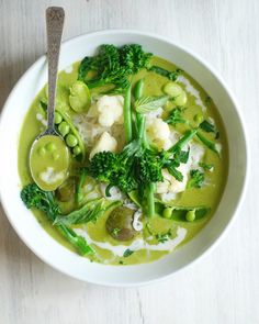 a white bowl filled with broccoli, cauliflower and other vegetables next to a spoon