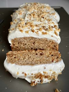 a loaf of carrot cake with white frosting and walnuts on top, sitting on a cutting board