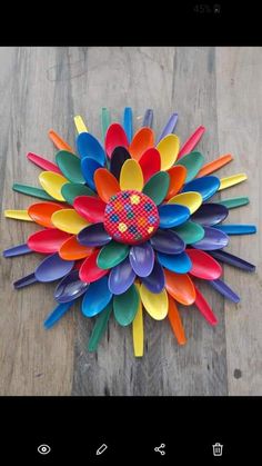 a colorful flower made out of plastic spoons on top of a wooden table next to a cell phone