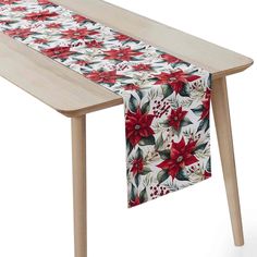 a table runner with poinsettis and holly leaves on it, sitting on top of a wooden table