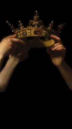 two hands holding up a golden crown against a black background with only one hand visible