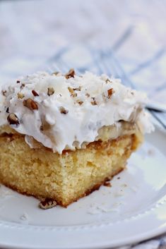 a piece of cake with white frosting and nuts on top sitting on a plate