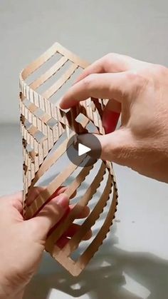 two hands are holding an object made out of strips of wood and plywood paper