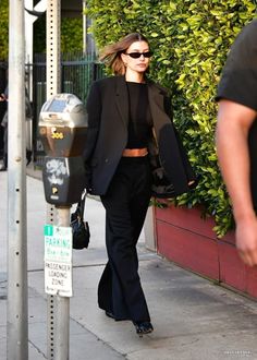 a woman walking down the sidewalk next to a parking meter