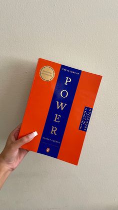 a person holding up a red book with the title power written in blue on it