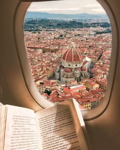 an open book sitting on top of a window sill next to a view of a city