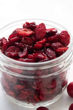 a glass jar filled with cranberries sitting on top of a white table next to some cherries