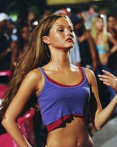 a woman with long hair standing in front of a crowd wearing a purple and red top