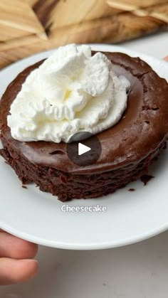 a person is holding a chocolate cake with whipped cream on top