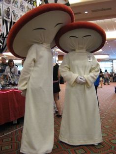 two people dressed in costume standing next to each other with large mushrooms on their heads