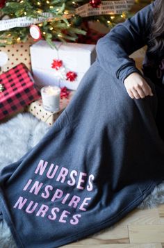 a woman laying on the floor in front of a christmas tree wearing a nurse's inspire nurses shirt