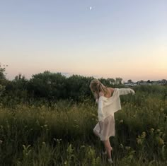 a woman standing in the middle of a field with her arms spread out and looking at the sky