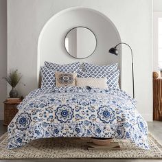 a bed with blue and white flowers on it in front of a round mirror above the bed