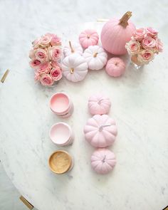 pink flowers and pumpkins are arranged on a white marble table with gold rimmed dishes