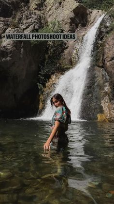 a woman standing in the water near a waterfall