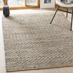 a large rug in the middle of a room with a chair and vase on the floor