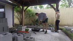 two people are working in the yard with cement blocks and plants on the ground,