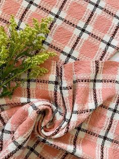 a pink and white checkered blanket with flowers on it, next to a plant