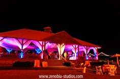 an outdoor wedding venue lit up with purple and white lights at night time for the reception