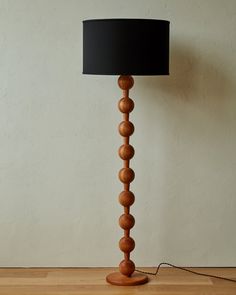 a wooden floor lamp with a black shade on the base and a cord attached to it