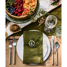 a place setting with green napkins and silverware on a wooden table top, surrounded by fruit