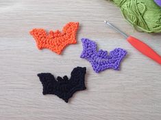 three crocheted bats sitting on top of a table next to yarn and knitting needles