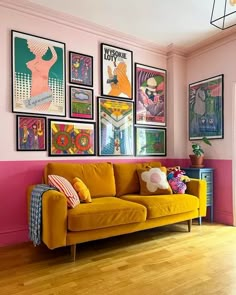 a yellow couch sitting in front of a pink wall with posters on it's walls