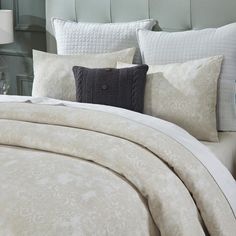 a bed with white and beige comforters and pillows on top of it, next to a night stand